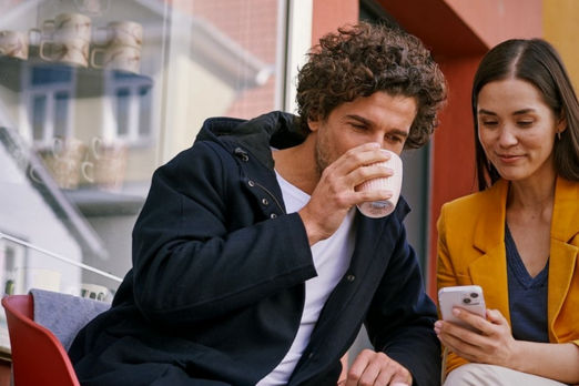 Sitzendes Paar vor einem Cafe mit dem Handy in der Hand