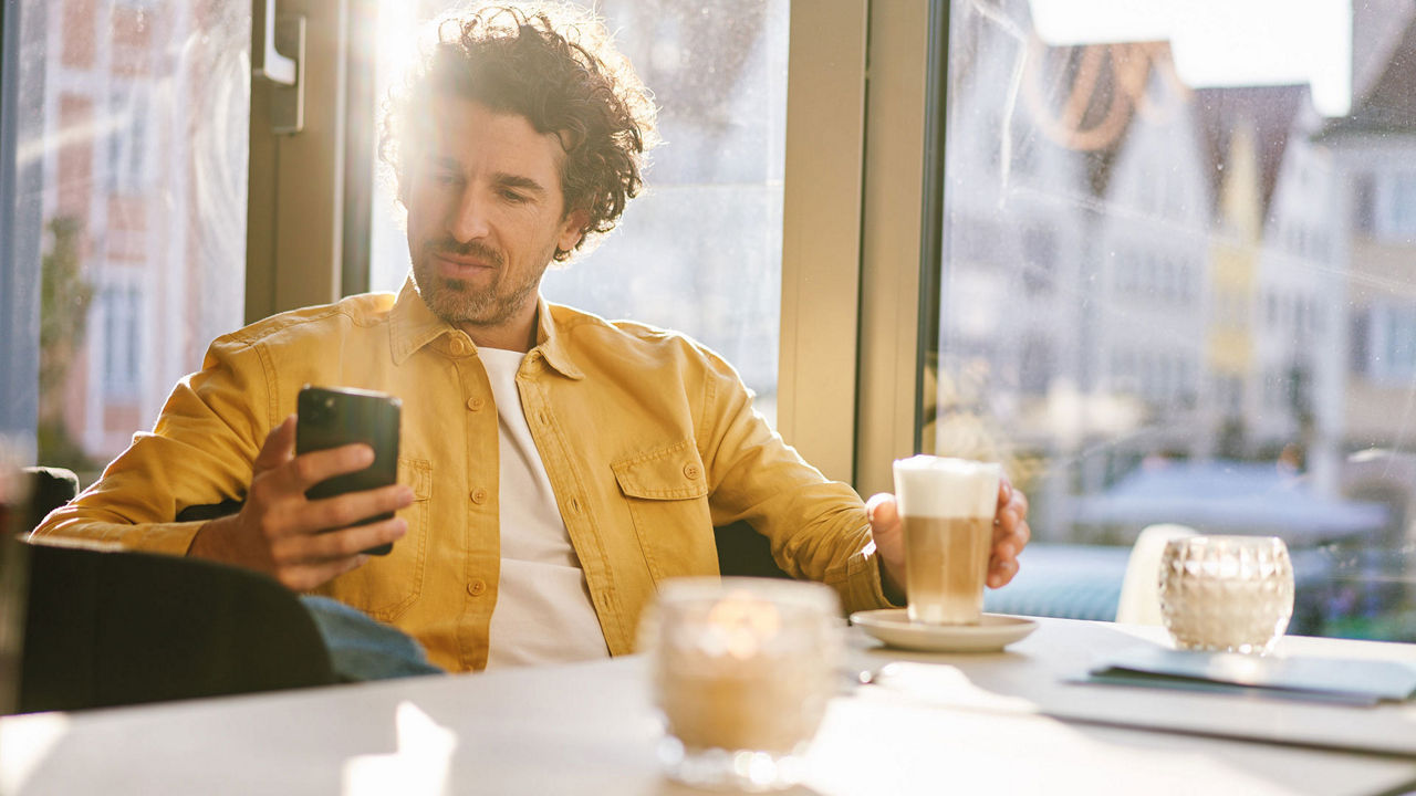 Ein Mann schaut auf sein Handy und sitz in einem Café bei einem Kaffee