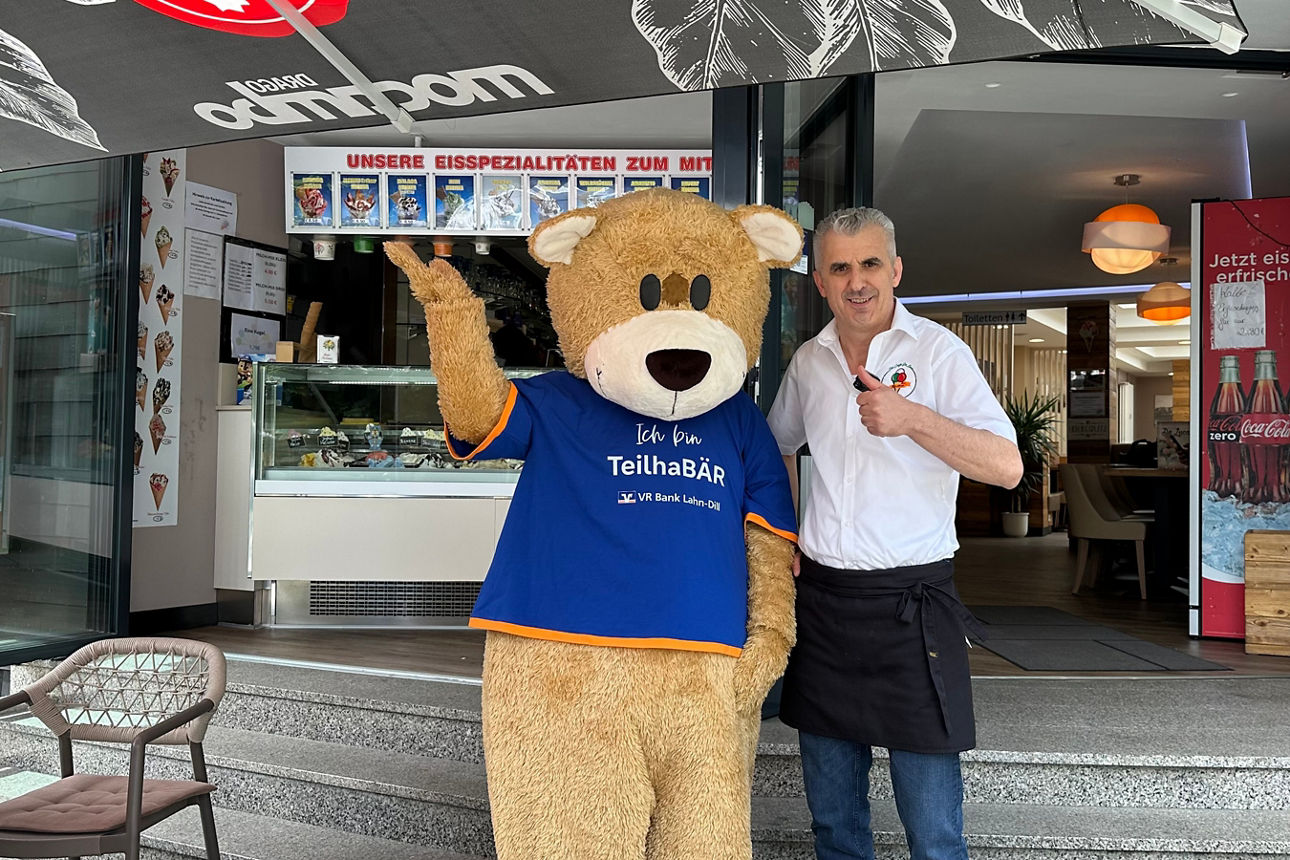 Mann steht neben Bärenkostüm vor einem Eiscafé