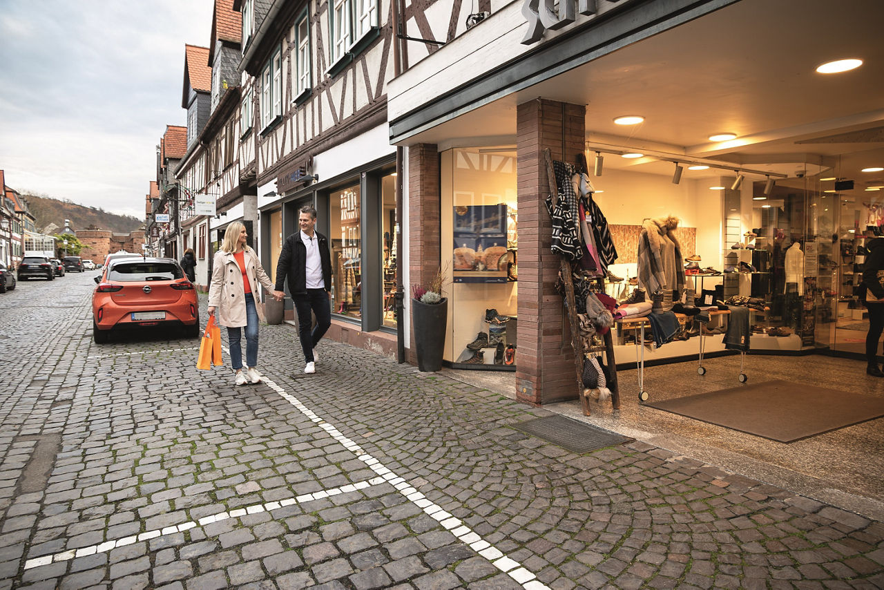 Eine Frau und ein Mann lächeln sich an und laufen Hand in Hand durch eine Einkaufsstraße.