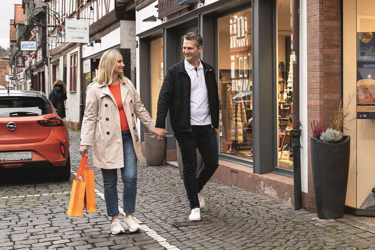 Eine Frau und ein Mann lächeln sich an und laufen Hand in Hand durch eine Einkaufsstraße.