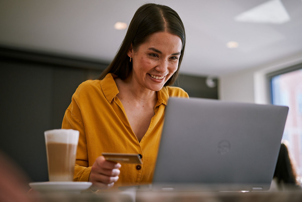 Frau sitzt im Café am Laptop und shopt online, in der Hand hält sie ihre girocard.