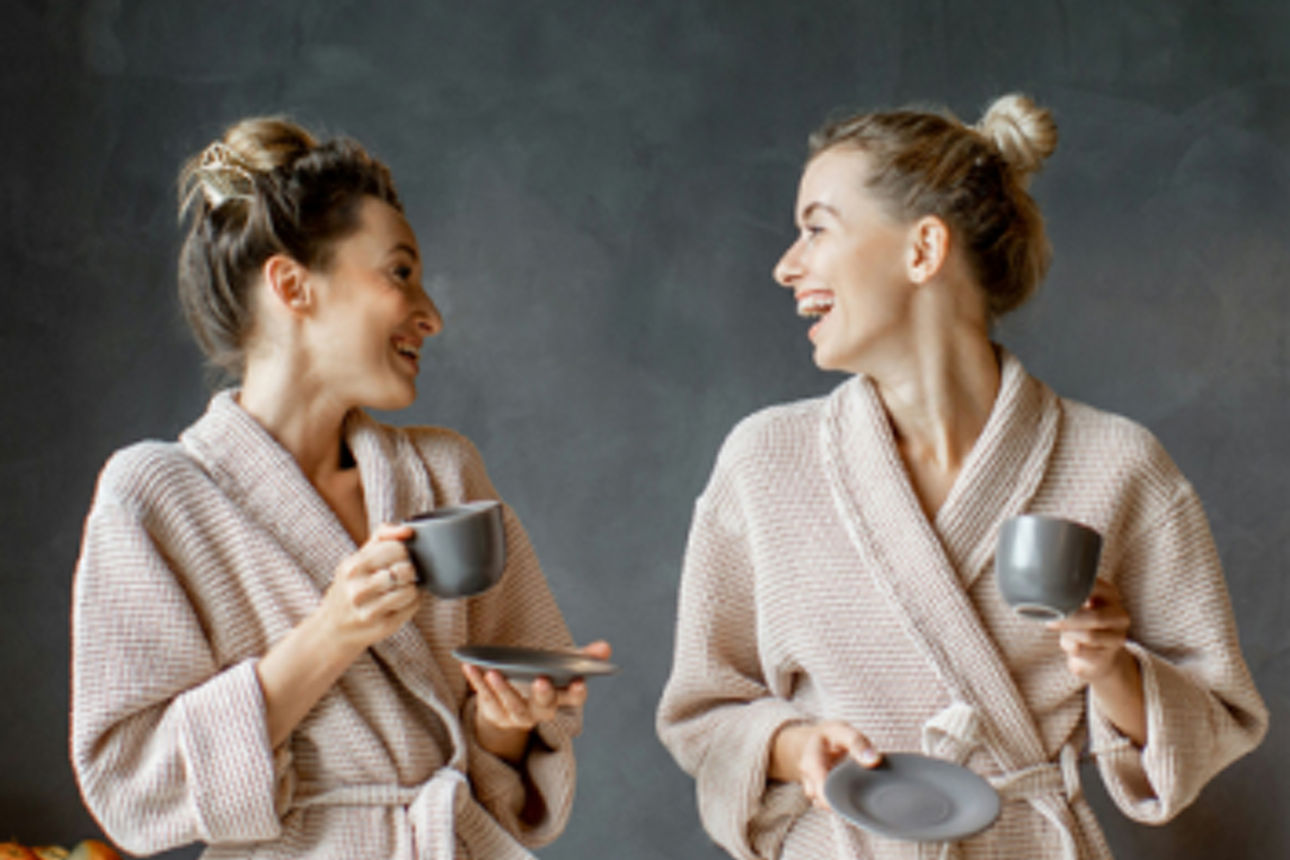 Zwei lächelnde junge Damen im Bademantel trinken Kaffee