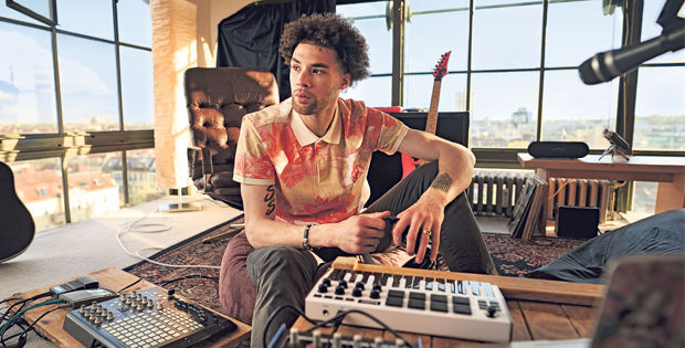 Junger Mann sitzt in einem Wohnzimmer mit Musikequipment