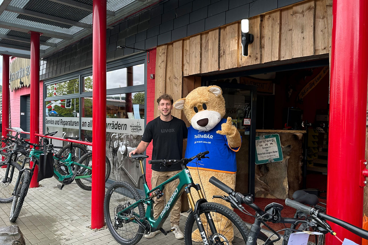 MeinPlus Cashback, Mann steht mit Fahrrad neben einer großen Bärenmaskottchen vor einem Fahrradgeschäft.