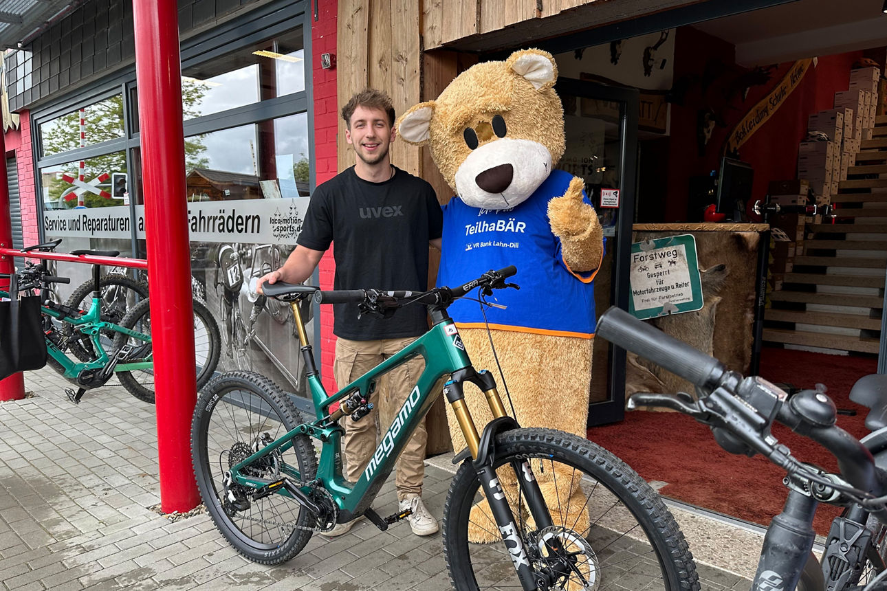 MeinPlus Cashback, Mann steht mit Fahrrad neben einer großen Bärenmaskottchen vor einem Fahrradgeschäft.