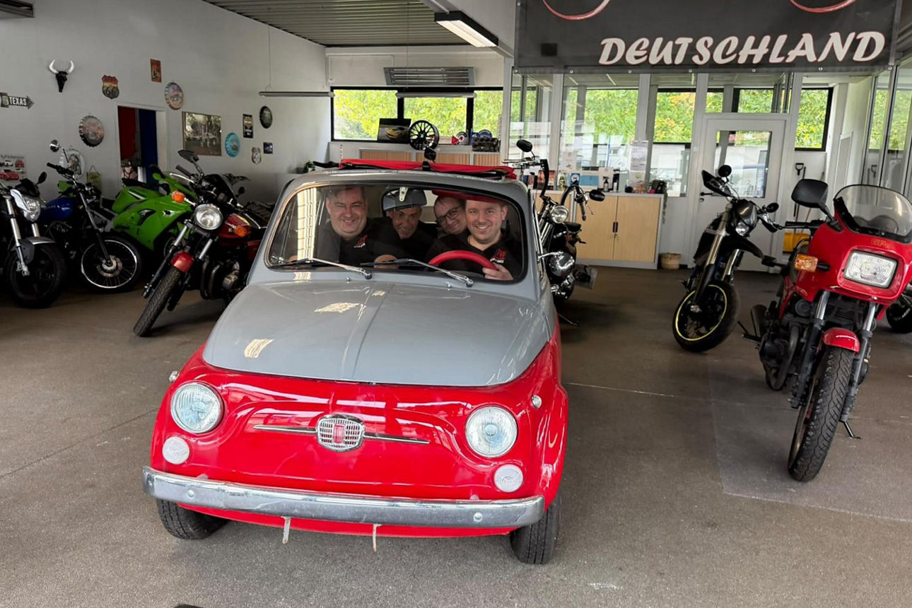 Vier Männer sitzen lachend in einem kleinen roten Auto
