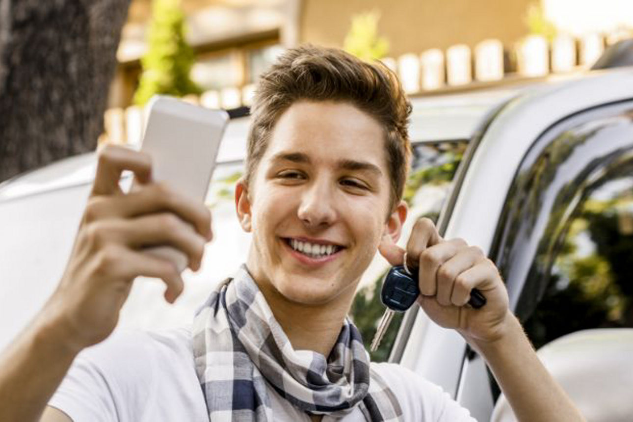 Junger Mann macht ein Selfie mit einem Autoschlüssel vor einem Auto