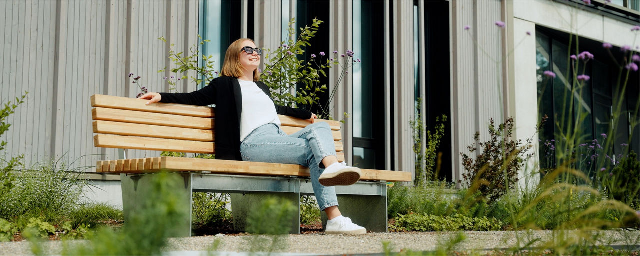 Frau sitzt mit Sonnenbrille auf Bank und schaut in die Sonne