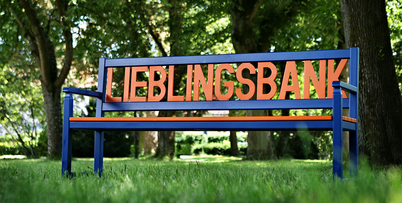Eine aus Holzgeschnitzte Lieblingsbank stehend auf einer Wiese.