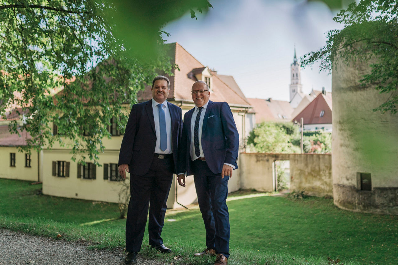 Zwei Männer vor einem Haus und grüner Wiese