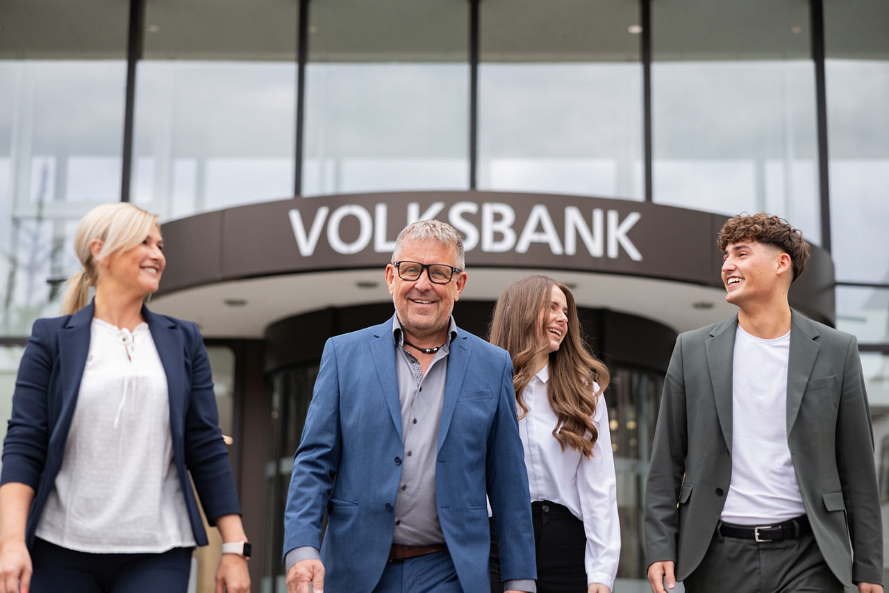 Mehrere Personen kommen gut gelaunt aus dem Eingang einer Volksbank.