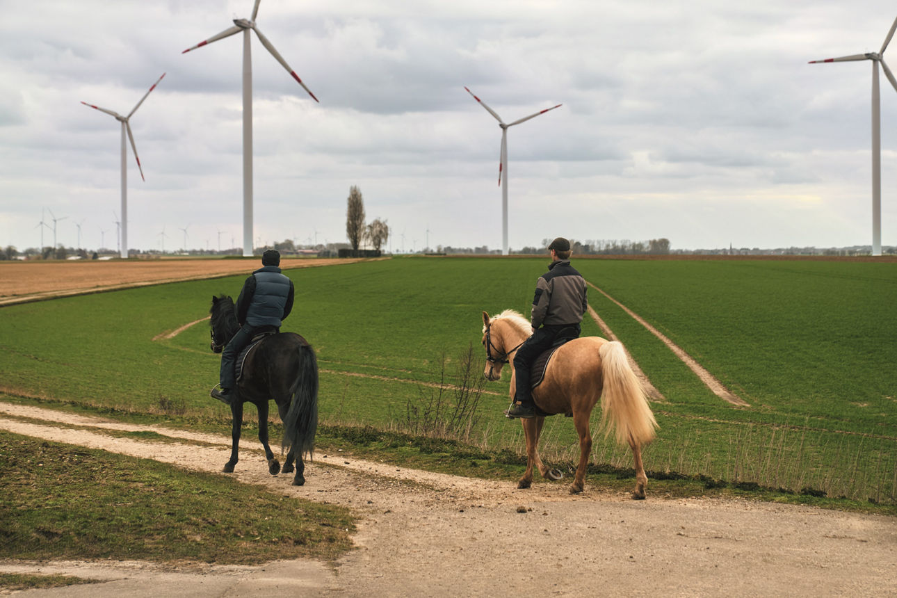 Zwei Reiter auf einem Feld mit Windrädern im Hintergrund