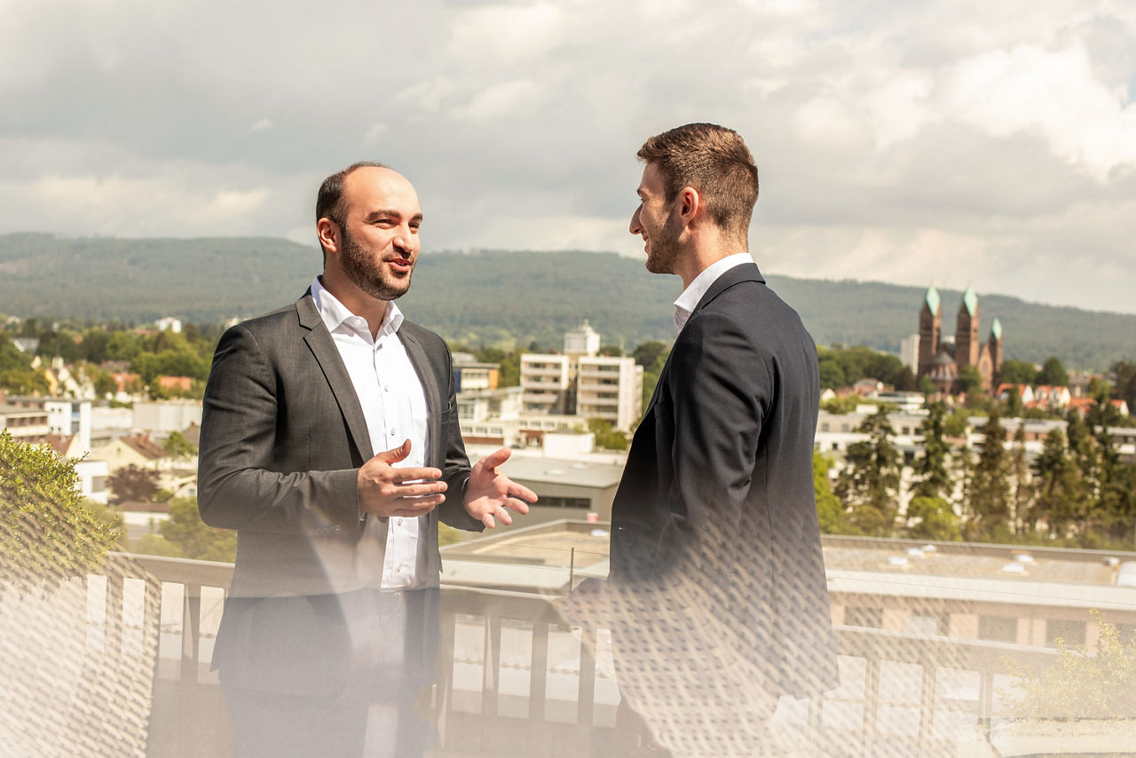 Abbildung zeigt zwei Mitarbeiter, die sich auf der Dachterrasse von Meine Bank unterhalten