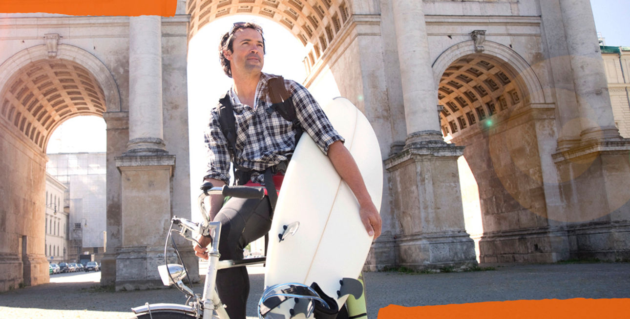Mann mit Surfbrett unterm Arm vor dem Siegestor in München