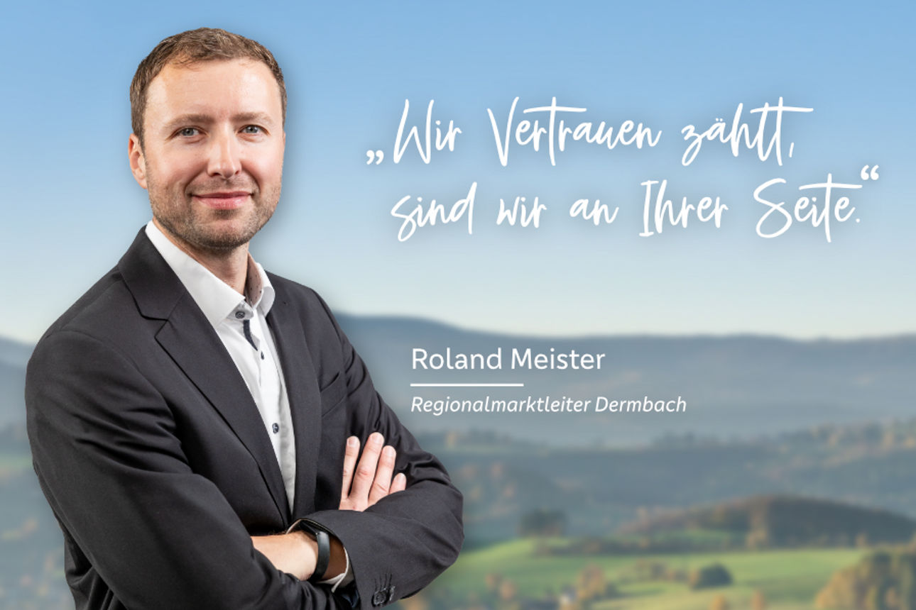 Bereichsleiter Privatkunden Roland Meister lachend vor einer Berglandschaft mit verschränkten Armen