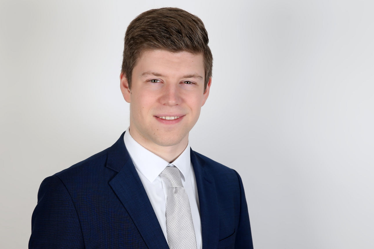 Ein lächelnder Mann in einem Anzug schaut in die Kamera.