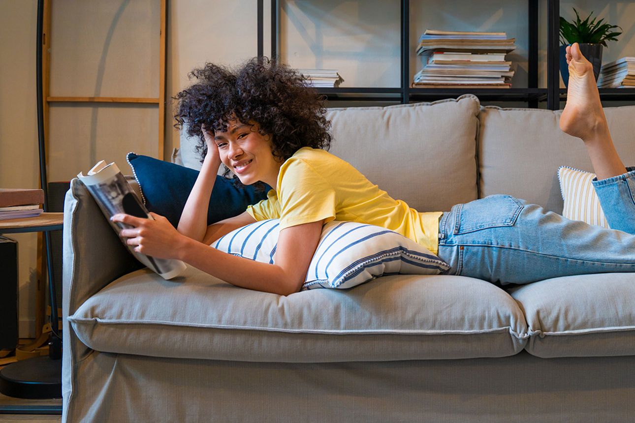 Eine junge Frau liegt auf einem Sofa und lächelt in die Kamera