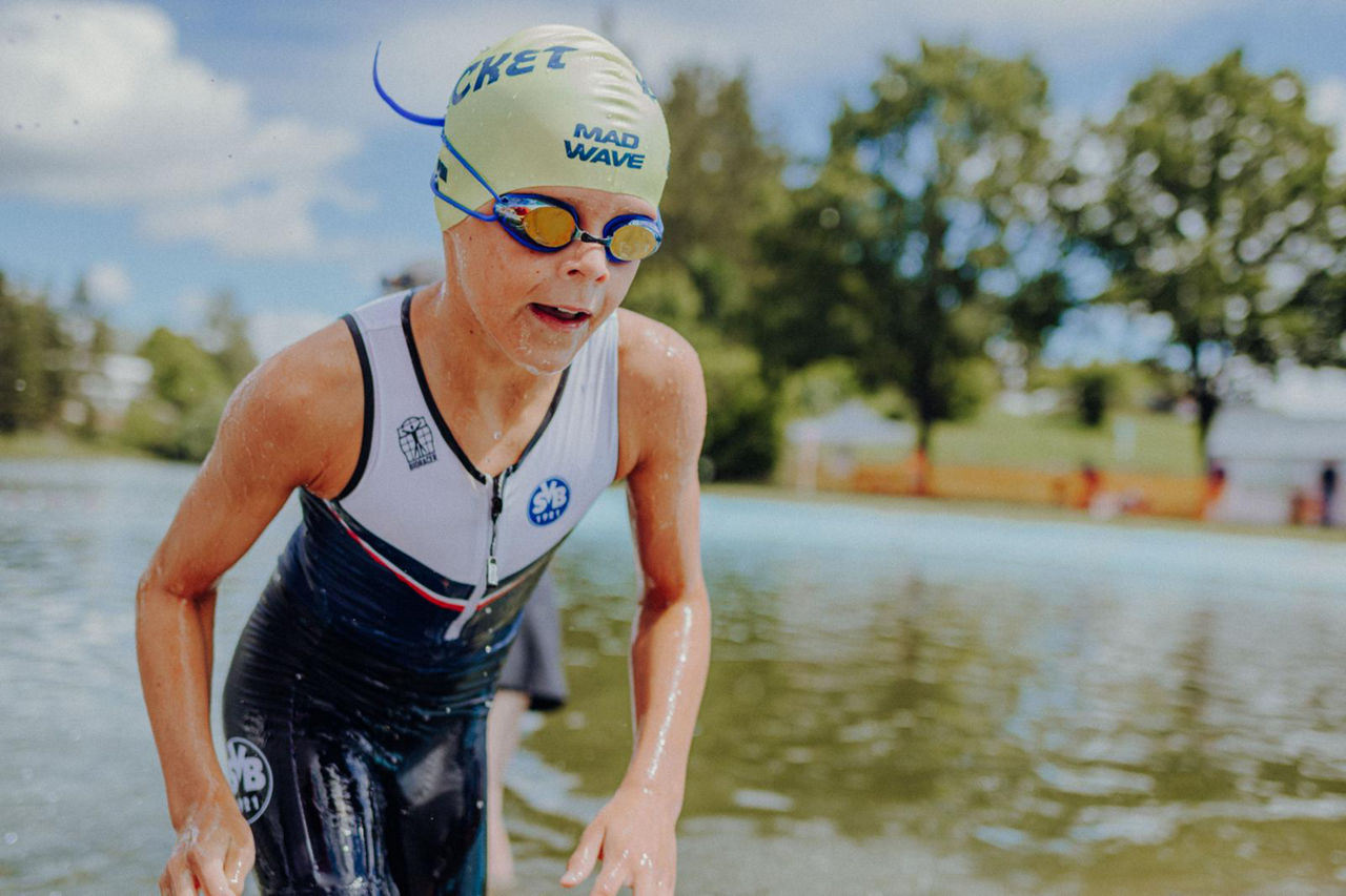 Schwimmer im Neoprenanzug verlässt das Wasser – sportliche Szene mit Badekappe und Naturkulisse