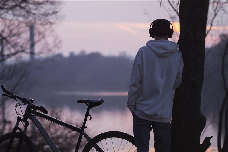 Junger Mann im weißen Hoodie hört Musik und bewundert die Natur. Er fährt Fahrrad.