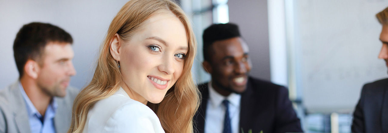 Geschäftsfrau mit ihren Mitarbeitern, Personengruppe im Hintergrund in einem modernen, hellen Büro im Innenbereich