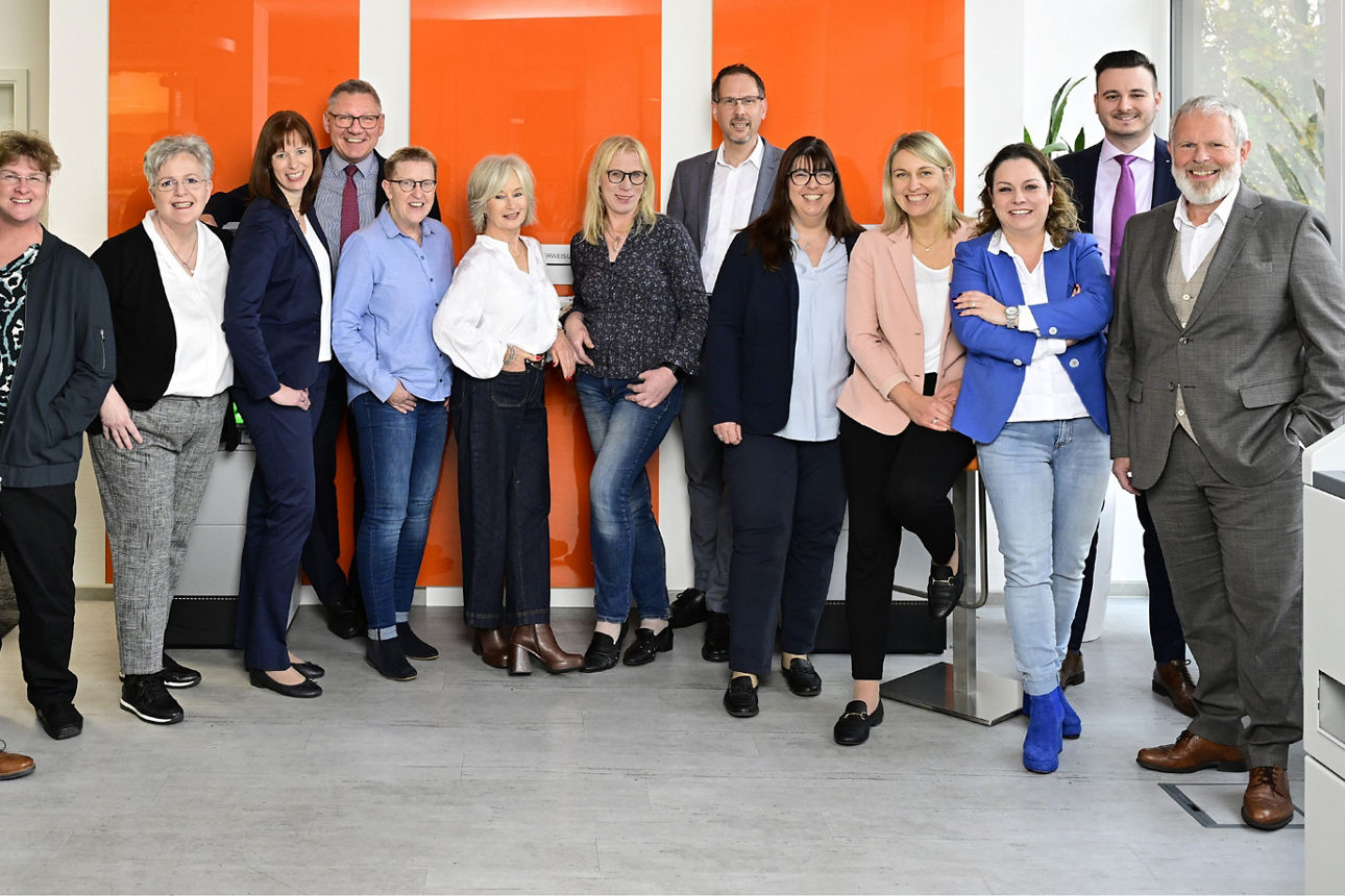 Eine vielfältige Gruppe von Menschen steht gemeinsam vor einem modernen Bürogebäude, lächelt und unterhält sich angeregt.  