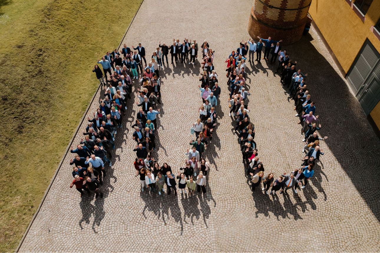 Luftbildaufnahme aller Mitarbeiterwelche die Zahl Einhundert bilden