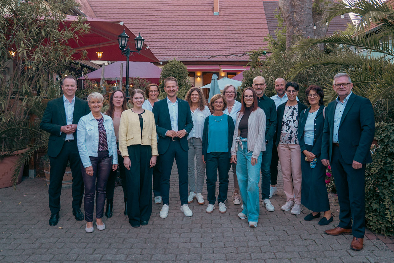 Gruppenfoto mit mehreren Personen in einem Innenhof vor einem Gebäude mit rotem Ziegeldach.