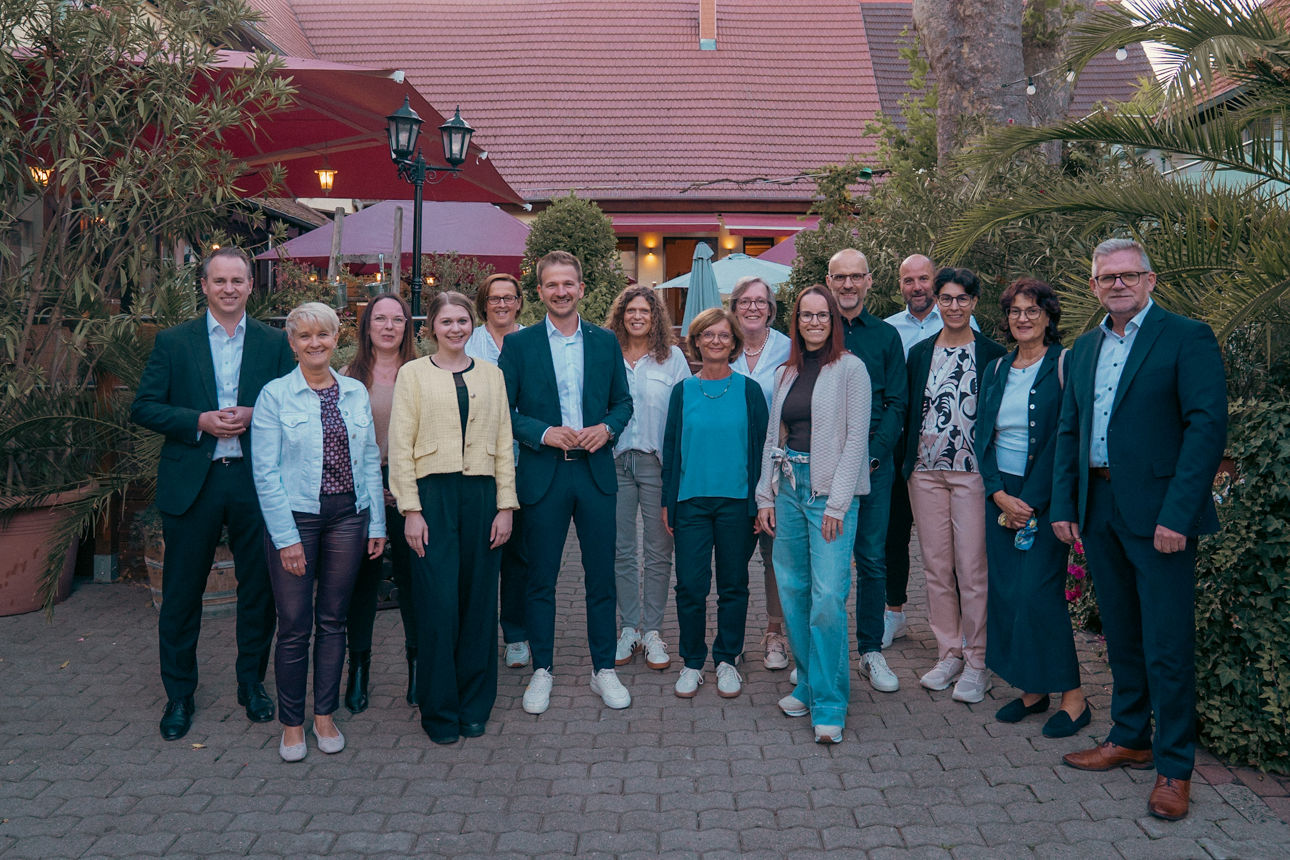 Gruppenfoto mit mehreren Personen in einem Innenhof vor einem Gebäude mit rotem Ziegeldach.