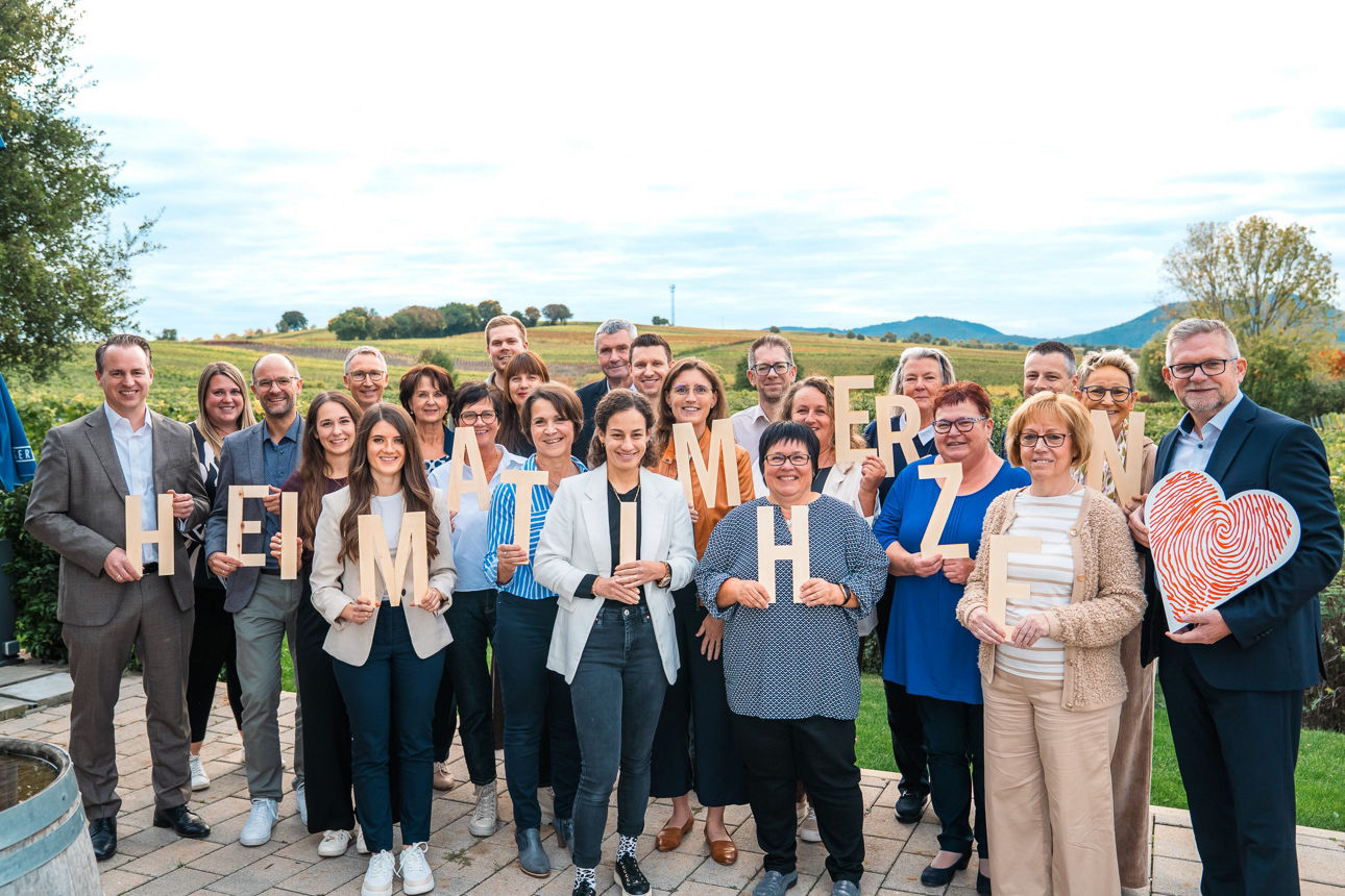 Gruppe von Menschen hält große Buchstaben hoch, die den Schriftzug ‚HEIMAT IM HERZEN‘ ergeben.