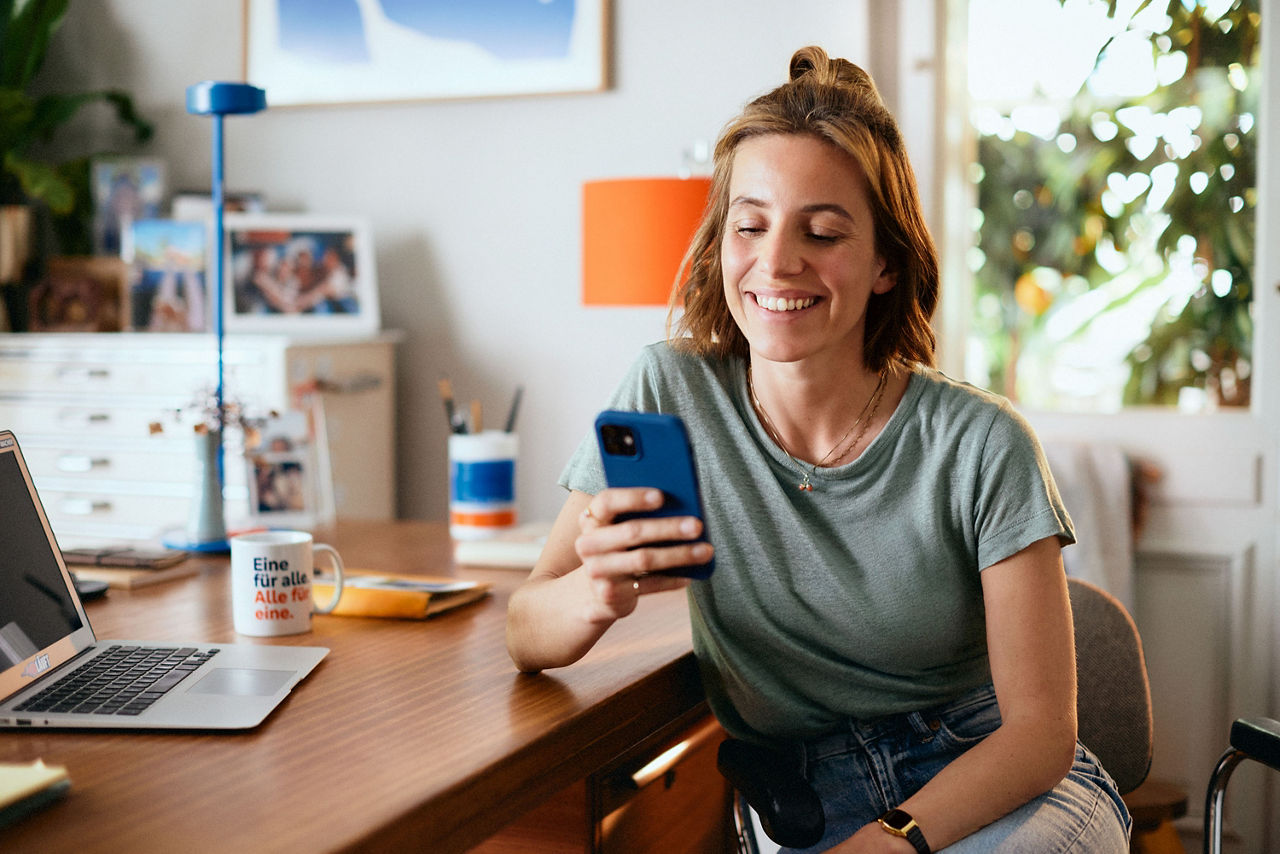 Junge Frau sitz am Schreibtisch und tippt am Handy