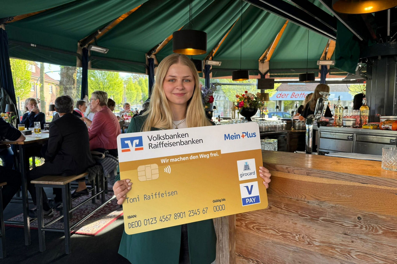 Frau mit einer großen Girocard in der Hand steht in einer Schirmbar