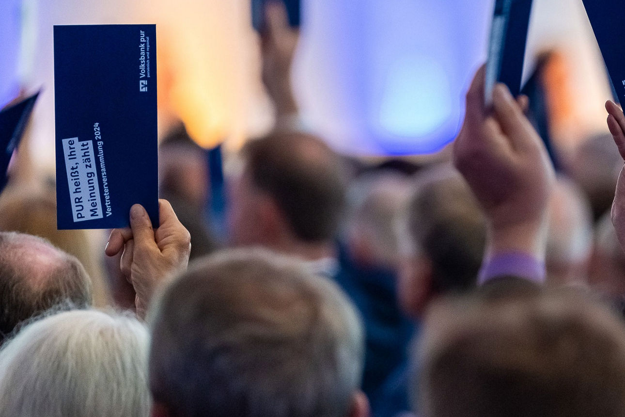 Sitzende Personen im Raum die per Karte abstimmen.