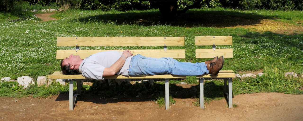 Mann liegt mit dem Rücken auf einer Bank im Park bei schönem Wetter