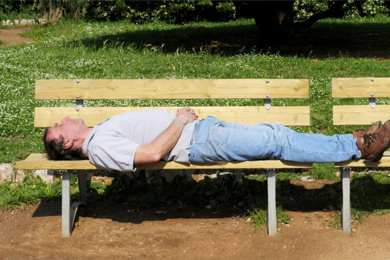 Mann liegt mit dem Rücken auf einer Bank im Park bei schönem Wetter