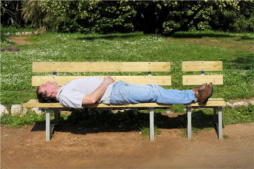 Mann liegt auf dem Rücken auf einer Bank im Park bei schönem Wetter