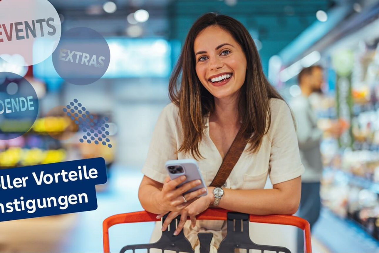 Frau mit braunen Haaren steht am Einkaufwagen und hält eine Smartphone in einem Supermarktgang.