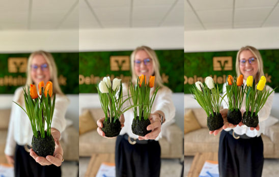 Eine Mitarbeiterin vor dem Heimatbank Logo mit Tulpen in der Hand