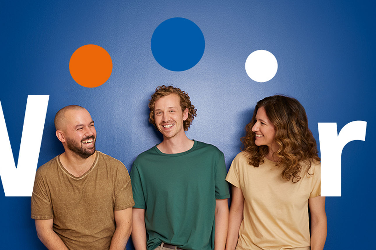 Drei lachende Menschen stehen vor einer blauen Wand mit dem Schriftzug „Wir sind meine Bank.”