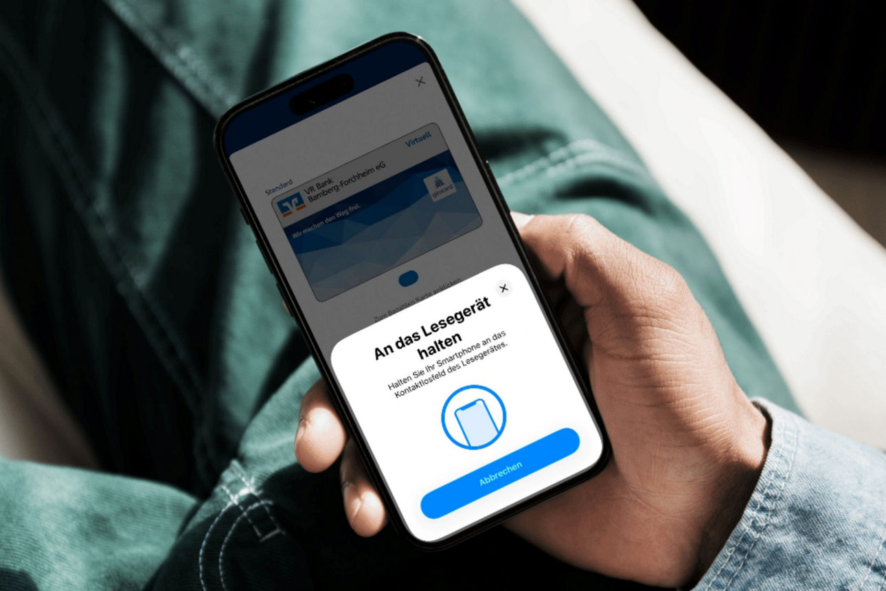 Junger Mann hält Smartphone mit VR Banking App und mobilem Bezahlvorgang in der Hand