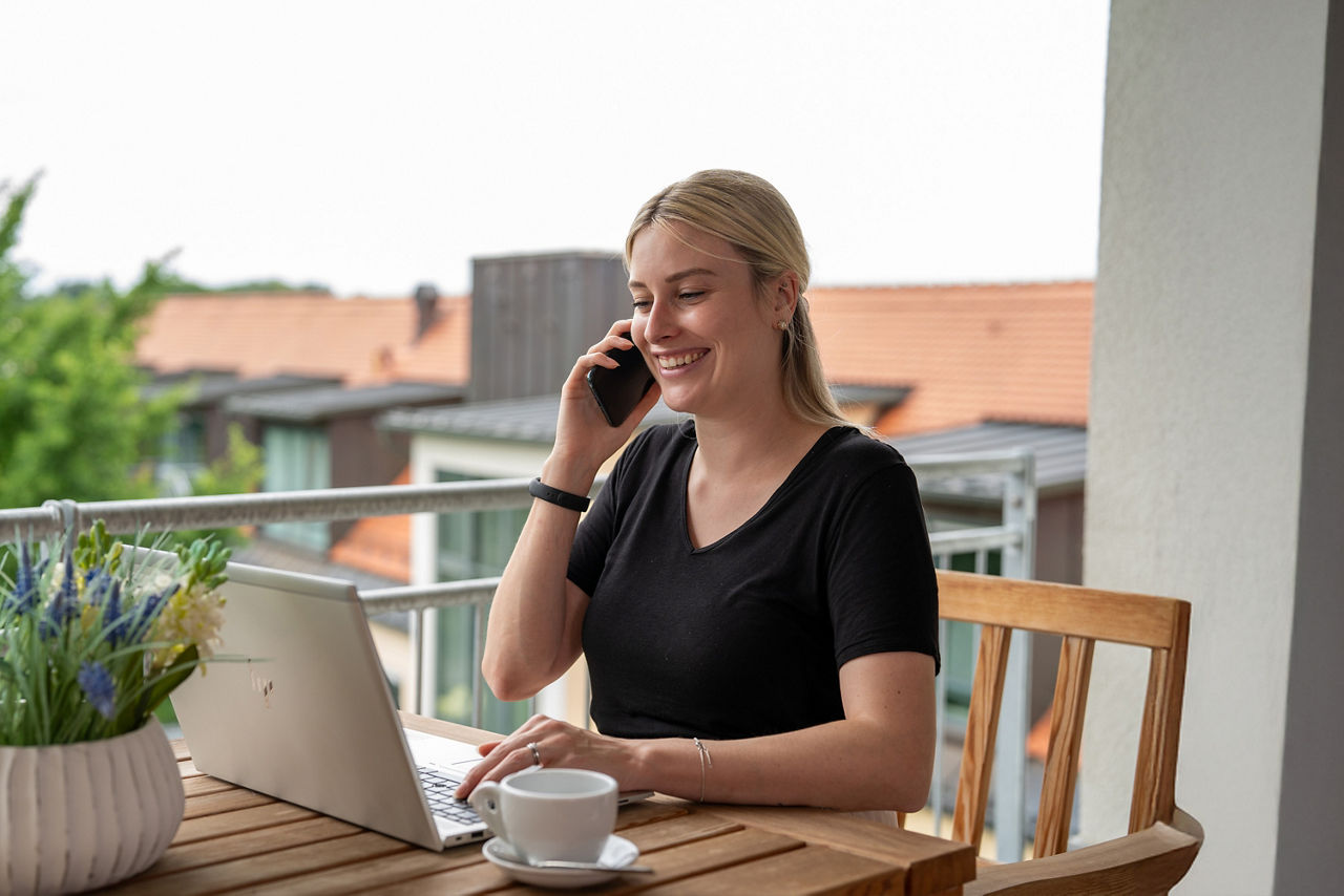 Frau sitzt an einem Tisch am PC und telefoniert