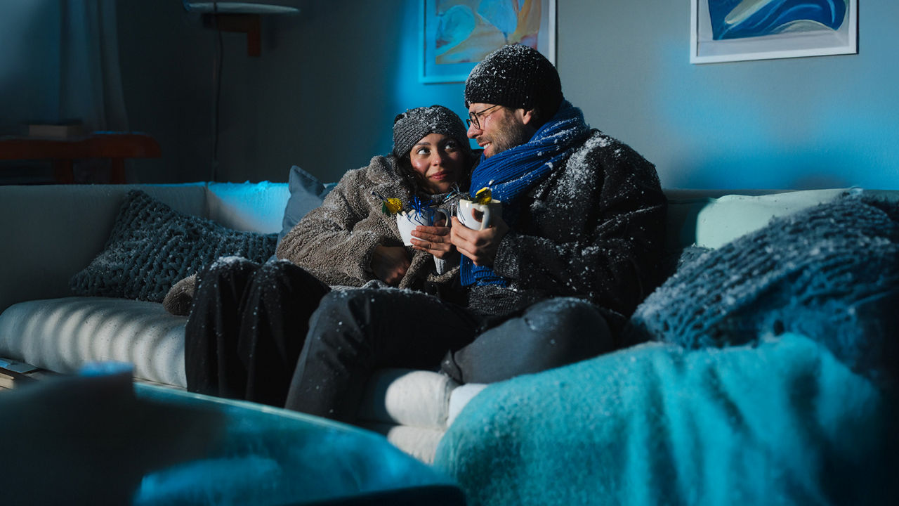 Ein junges Pärchen sitzt auf dem Sofa, es schneit im Haus