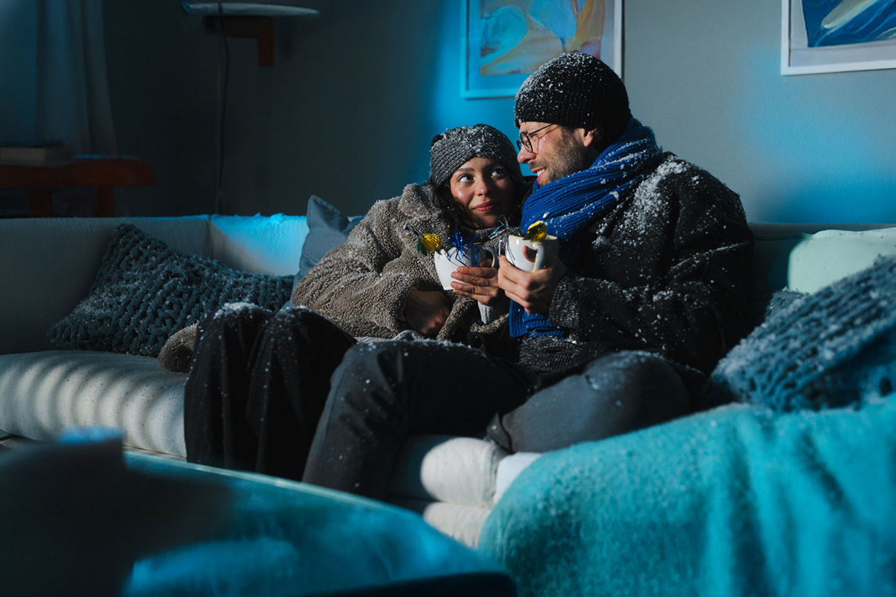 Ein junges Pärchen sitzt auf dem Sofa, es schneit im Haus