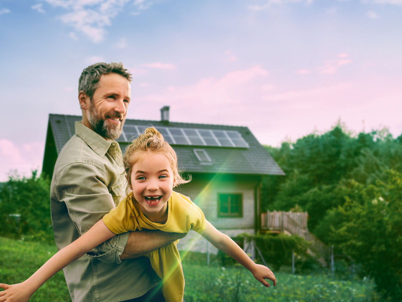 Mann hält ein Kind im Arm vor einem Haus mit Solaranlage