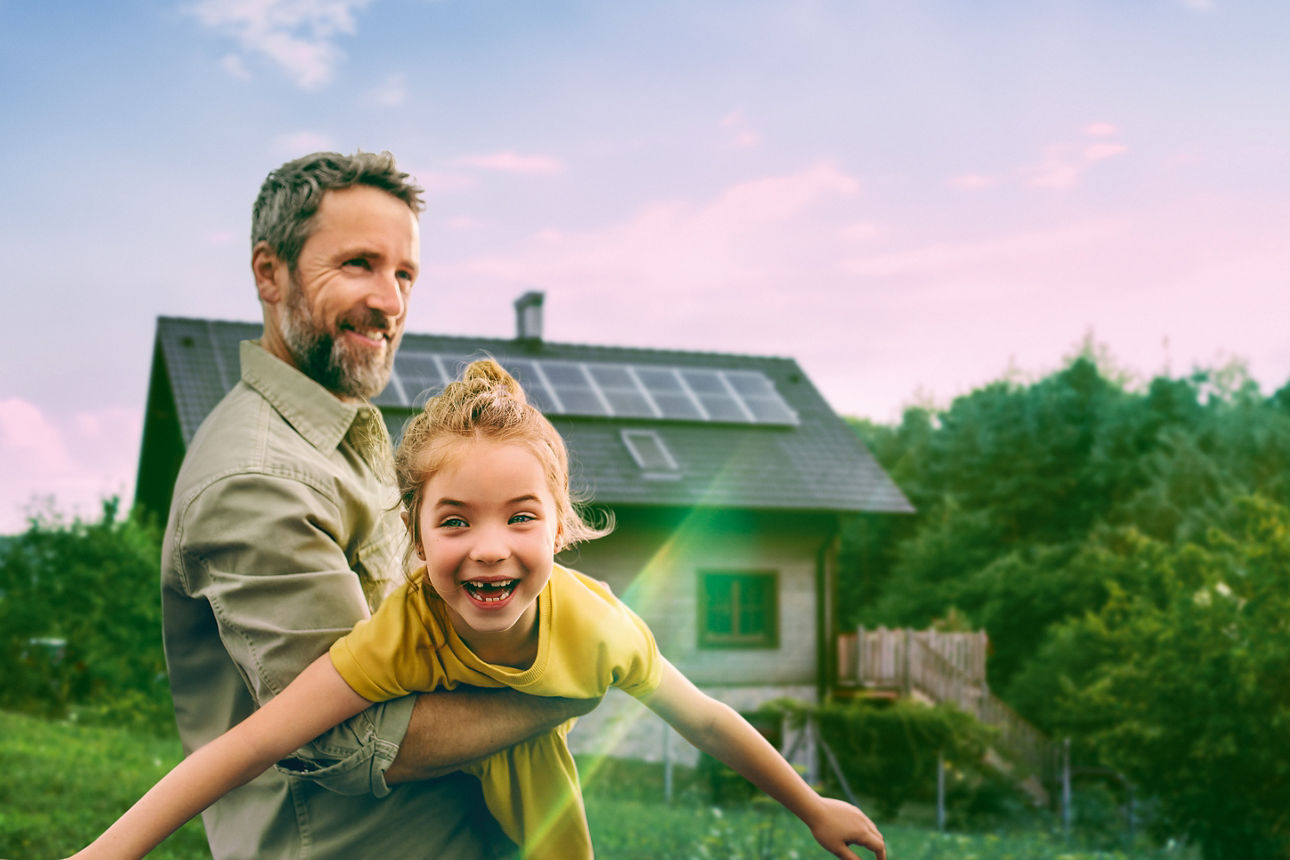 Mann hält ein Kind im Arm vor einem Haus mit Solaranlage