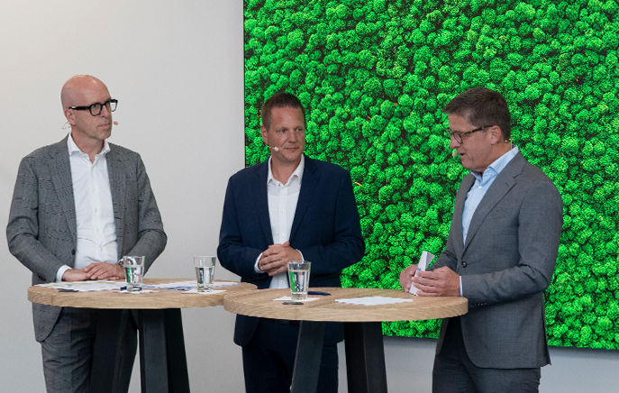 3 Männer in einem Symposium vor grüner Wand
