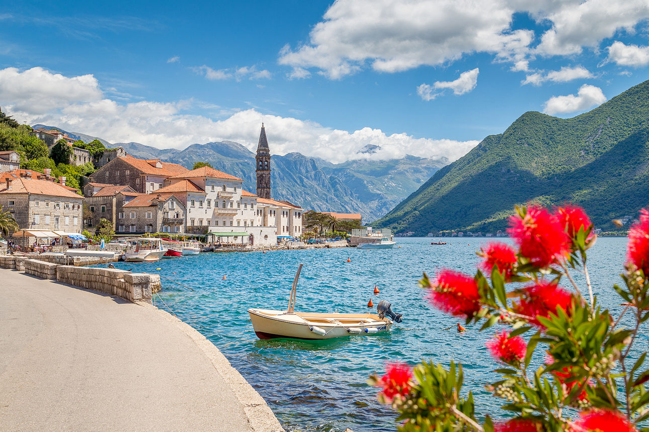 Bild zeigt einen verträumten Ort an einem Gewässer mit Bergen im Hintergrund