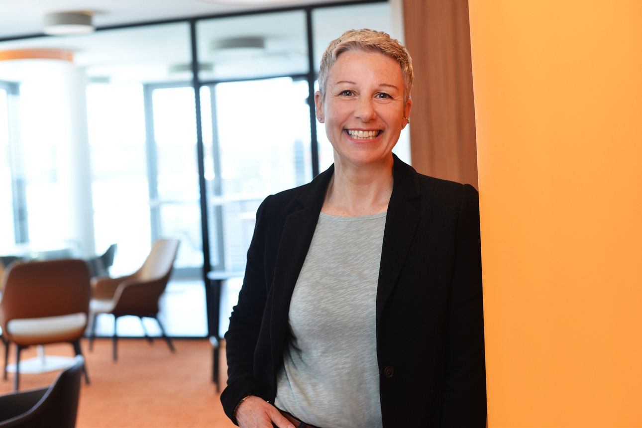 Ein Frau lehnt an der Wand und lächelt in die Kamera