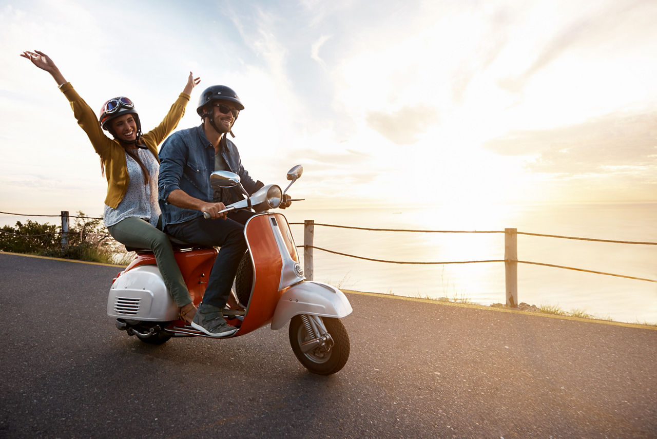Junge Frau, die ihre Arme ausstreckt, während sie mit ihrem Freund auf einem Motorroller fährt