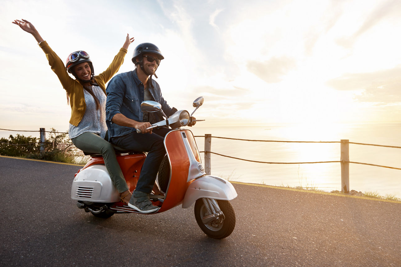 Junge Frau, die ihre Arme ausstreckt, während sie mit ihrem Freund auf einem Motorroller fährt